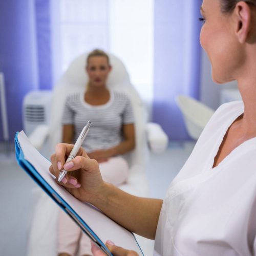 Doctor writing medical reports while talking to patient at clinic