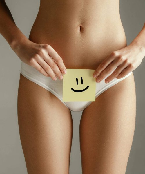 Woman health. Female model holding card near stomach. Young adult girl with paper sign or symbol of smile isolated on gray studio background. Cut out part of body. Medical problem and solution.